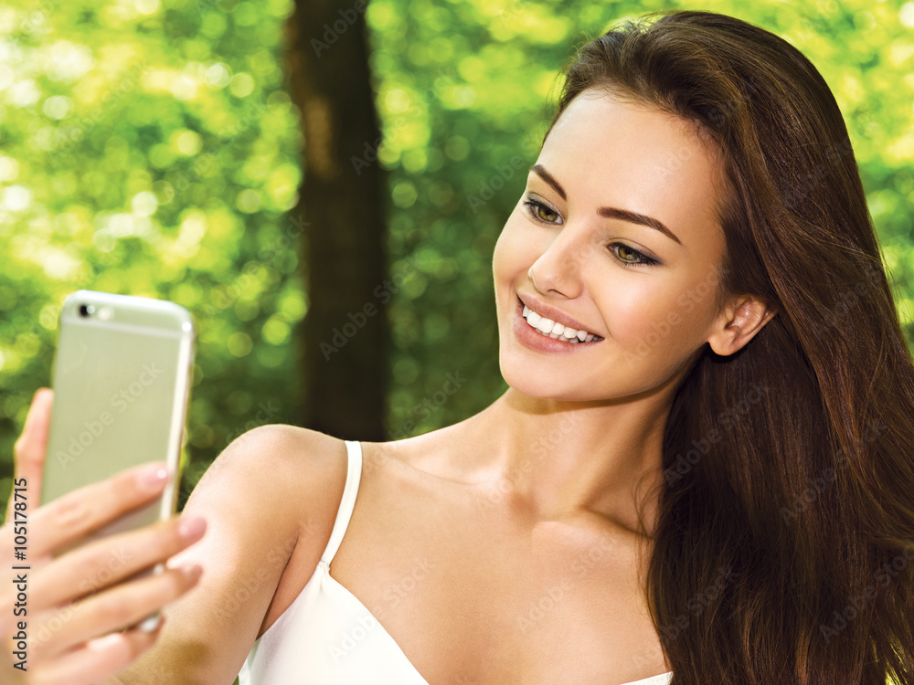 Naklejka premium beautiful young woman selfie in the park with a smartphone