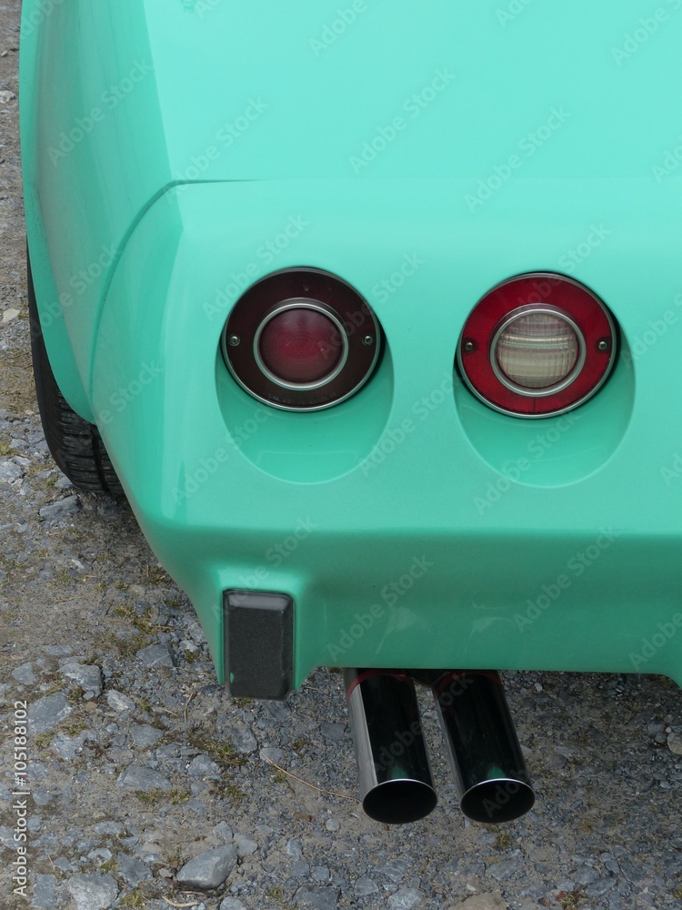 Naklejka premium Runde Rücklichter und verchromter Sportauspuff einer amerikanischen Sportwagen Ikone in Türkis auf grauem Schotter in Oerlinghausen bei Bielefeld im Teutoburger Wald in Ostwestfalen-Lippe