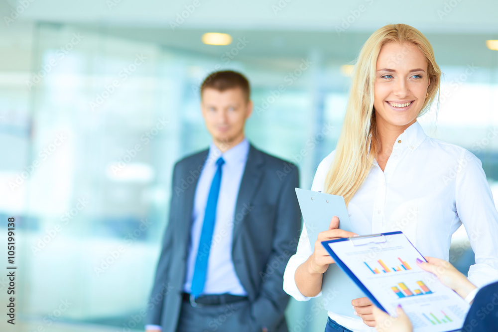 Portrait of young businesswoman in office with colleagues in the background Portrait of young businesswoman in office with colleagues in the background