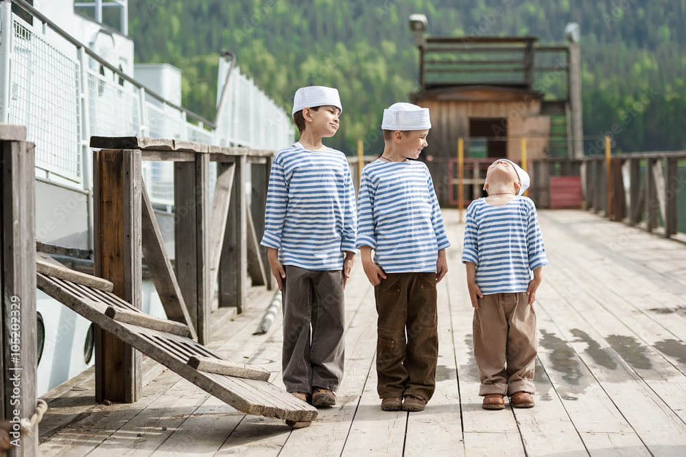 Three boys sailors on the pier of a mountain lake