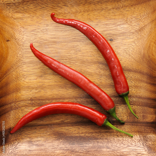 three cute red hot chili pepper on wood background
