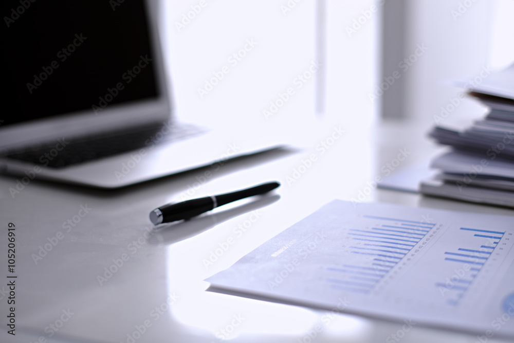 .Office workplace with a laptop and financial documents on the light reflecting table .Office workplace with a laptop and financial documents on the light reflecting table