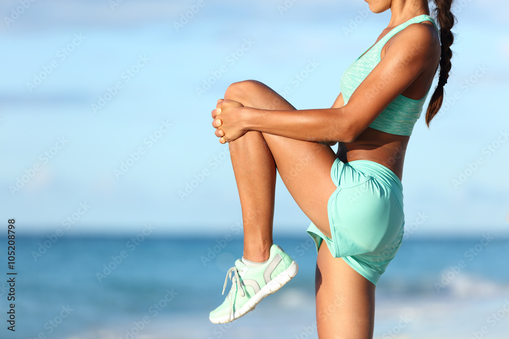 Fitness runner body closeup doing warm-up routine on beach before