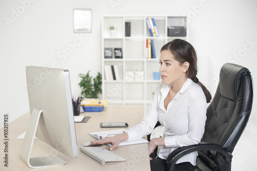 Business woman in office environment sitting in the chair and looking at computer monitor