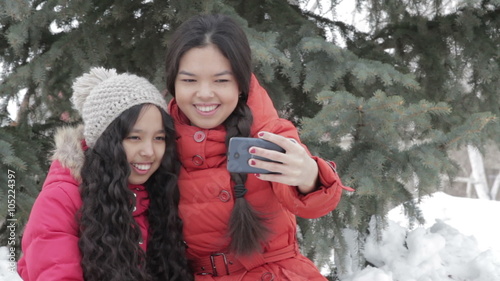 Smiling two girl taking a selfie with smartphone outdoors in warm clothes photo