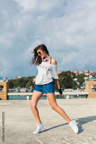 Fashion lifestyle portrait of young happy pretty woman having fun on the street at sunny day,listening favorite music at big earphones,stylish vintage outfit, bright fresh colors.white background