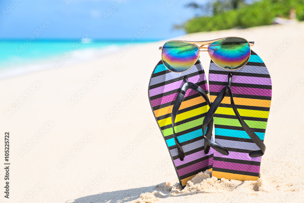 Multicolored flip-flops and sunglasses on a sunny beach..Tropica