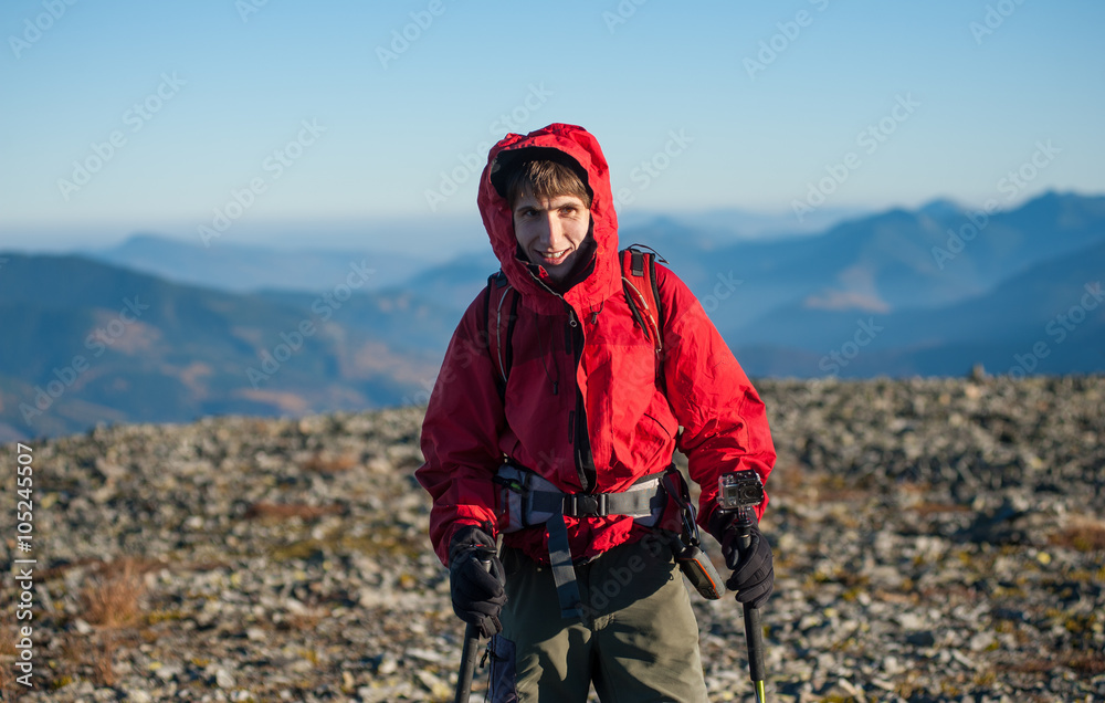 Portrait of male sportsman hiker on the top of the mountain. Man is wearing red jacket gloves and has trekking sticks and backpack on. Action camera attached to the walking stick. Portrait of male sportsman hiker on the top of the mountain. Man is wearing red jacket gloves and has trekking sticks and backpack on. Action camera attached to the walking stick.