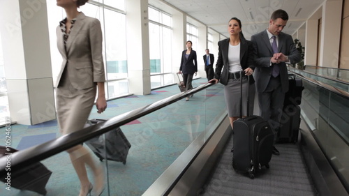 Business people at airport travel along moving walkway