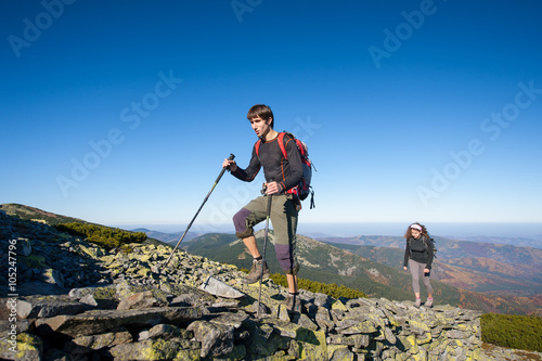 Young backpacker couple walking up rocky the mountain top, high altitude. Beautiful autumn mountain landscape on the background. Fall.