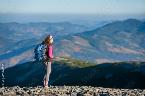 Young girl tourist is enjoying mountain plato with big backpack on. Beautiful mountains on background. Sunny fall day.