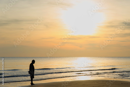 Man stand alone on the beach at sunset. Calm sea with waves.