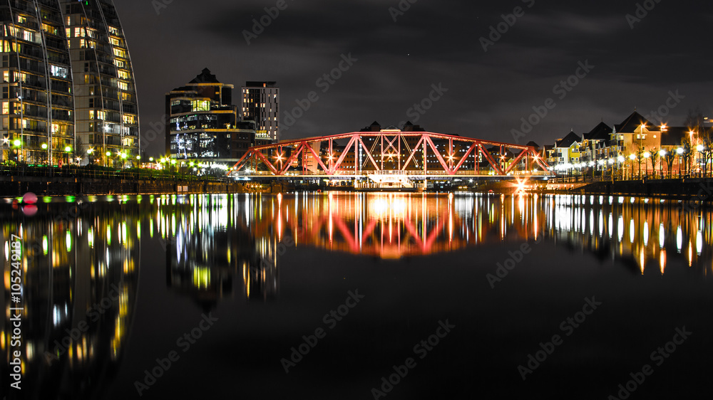 Fototapeta premium Reflections on a stale tranquil water at night from a highlighted industrial bridge in Salford, Manchester, United Kingdom