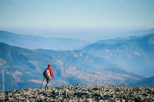 Climber is walking on the rocky mountain plato on backpacking trip. Beautiful mountains on background. Rear view. Ecotourism and healthy lifestyle concept. Copy space.