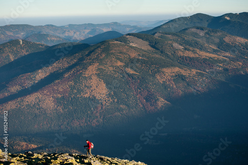 Young hiker walking on the rocky mountain against beautiful mountain on background, autumn colors. Side view. Ecotourism and healthy lifestyle concept. Copy space. Sunny fall day. Horizontal picture