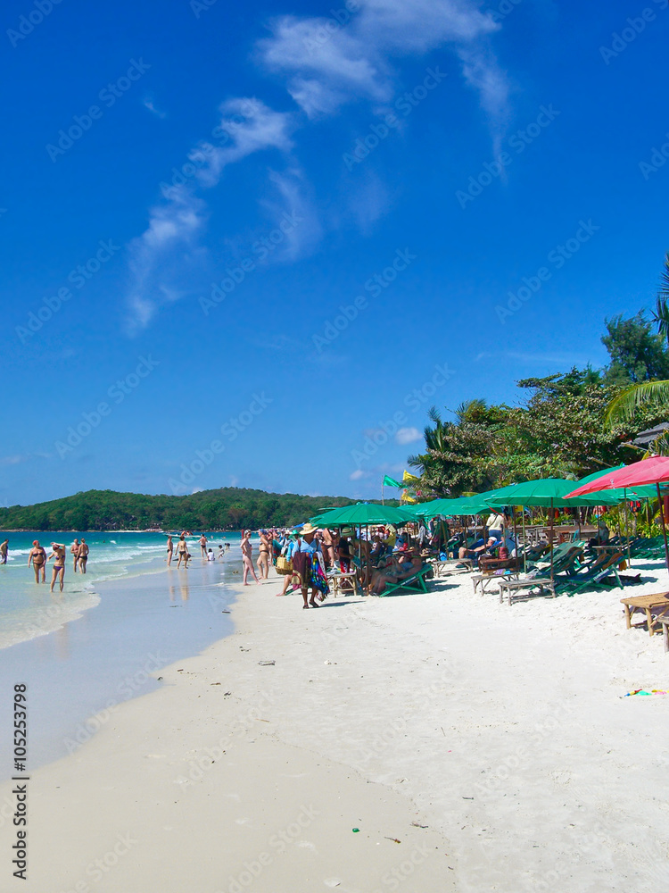 beautiful beach with idyllic beach chairs and sunshades. Tourist walking along the beach and swimming in the turquoise water. 