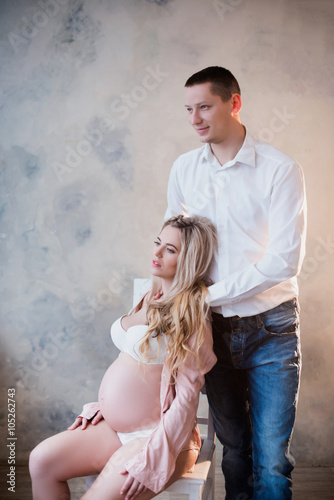 Husband hugging his pregnant wife in white lingerie on a light background, lifestyle, waiting, belly