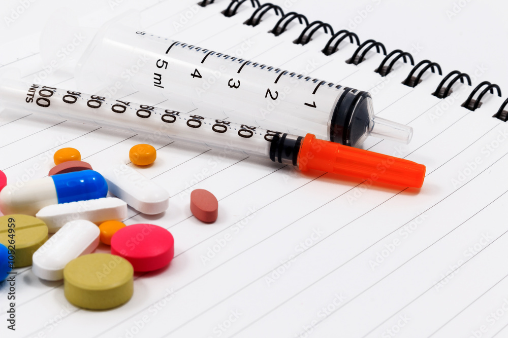 Syringes, sticky note and many colorful pills isolated on notebook. Syringes, sticky note and many colorful pills isolated on notebook.