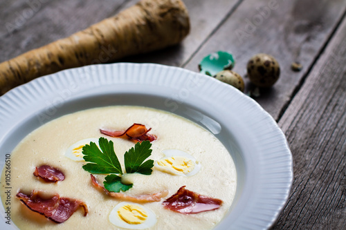 Creamy Horseradish soup with quail egg, black forest ham, decorated with leaf parsley. Soup in a deep plate on a gray wooden table.