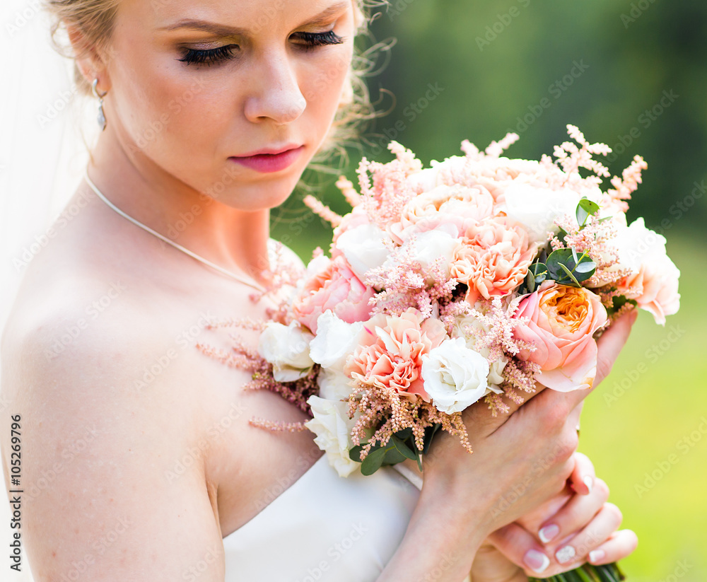 Naklejka premium Beautiful bride with wedding bouquet of flowers outdoors in green park.