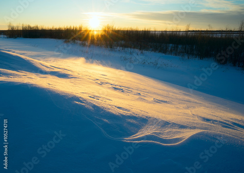 Winter landscape with the setting sun in  snowy field.