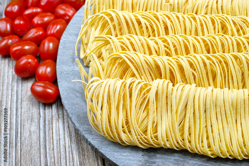 Homemade fettuccini pasta, small red tomatoes on wooden plate Stock