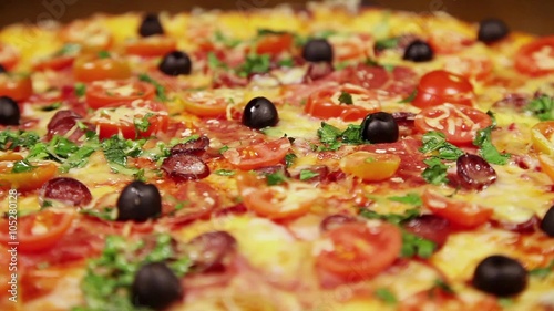 Low angle view video of rotating pizza with cheese, tomatoes and olives, close-up

