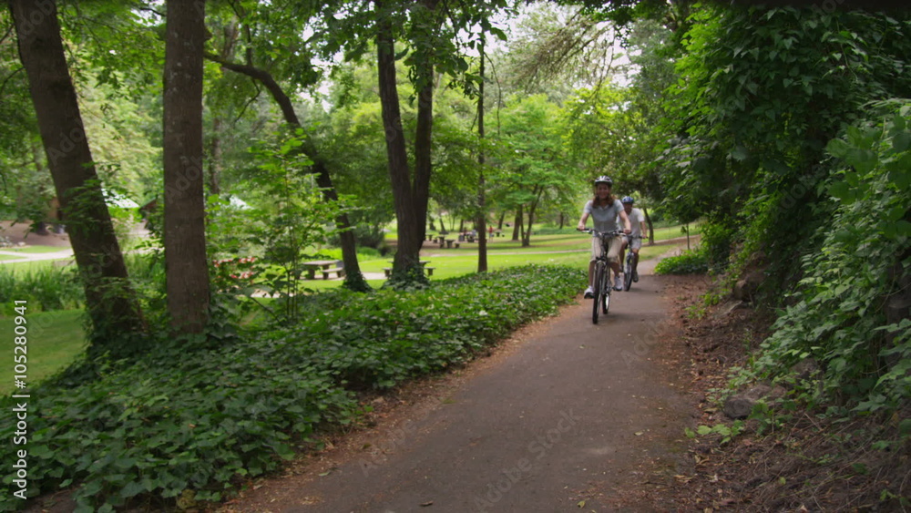 Mature couple riding bicycles at park, slow motion Mature couple riding bicycles at park, slow motion
