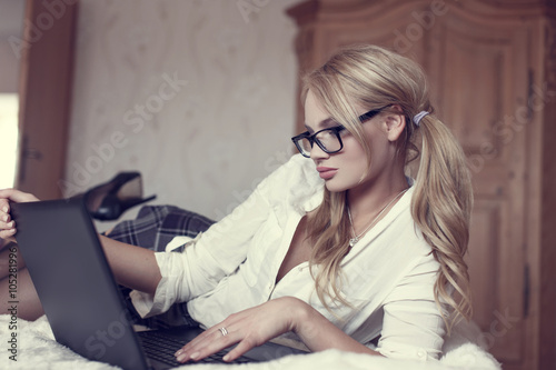 Sexy blonde woman in glasses on bed with laptop