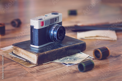 Old camera on an old book with photo rolls and pictures lying around photo