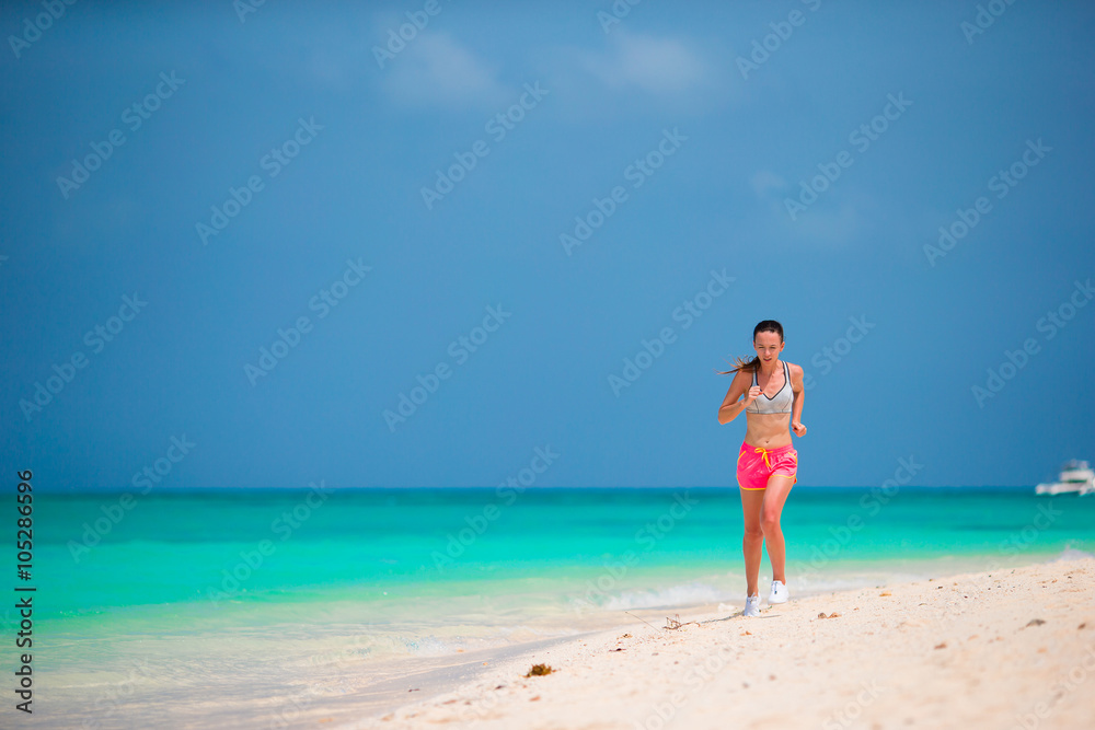 Fit sports young woman running along tropical beach in her sportswear 