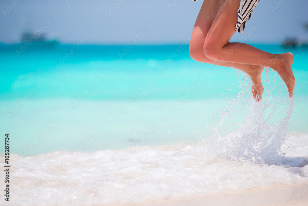Woman's feet on the white sand beach in shallow water