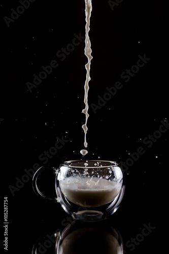 Pouring process of milk into a glass cup with reflection under glass cup, splashes and drops around glass cup