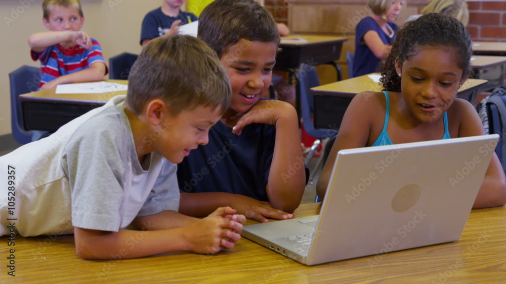 Three elementary school students look at laptop computer together