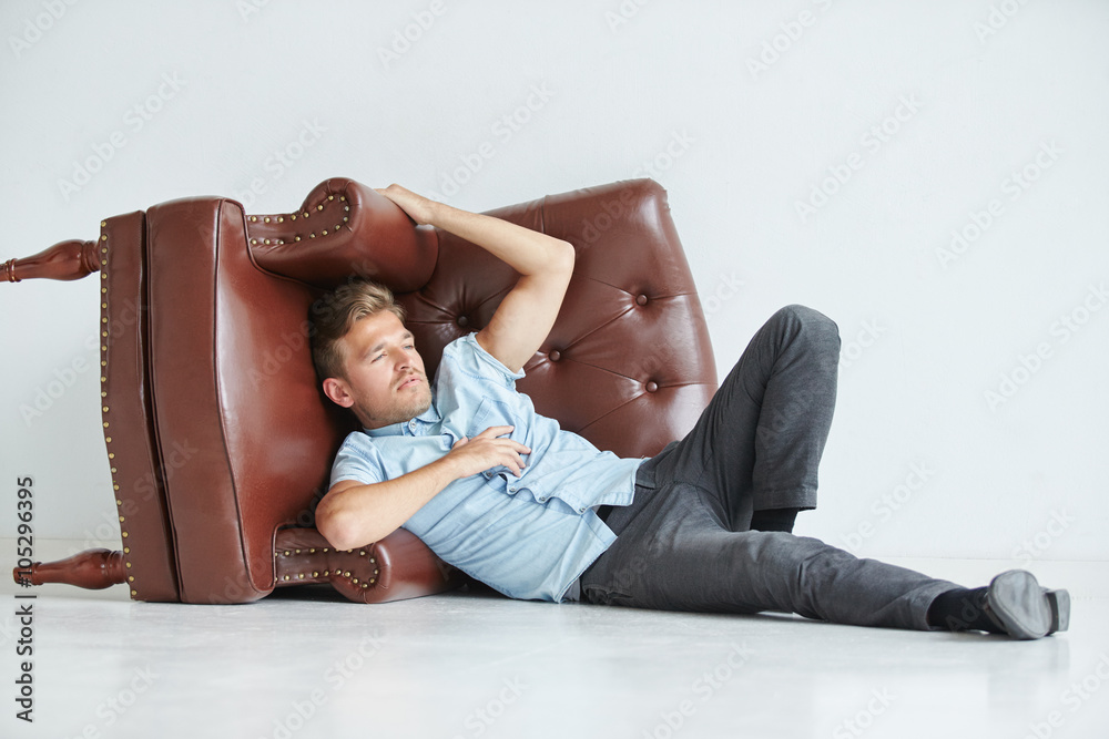 Brutal man lying next to a brown leather armchair , armchair lying on