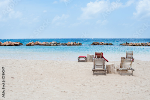wooden chairs on white sand beach with blue sky and water 