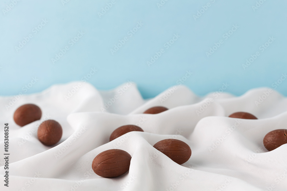 Chocolate Easter eggs among delicate white gauze fabric folds that looks like milk with copy space. Shallow depth of field. Chocolate Easter eggs among delicate white gauze fabric folds that looks like milk with copy space. Shallow depth of field.