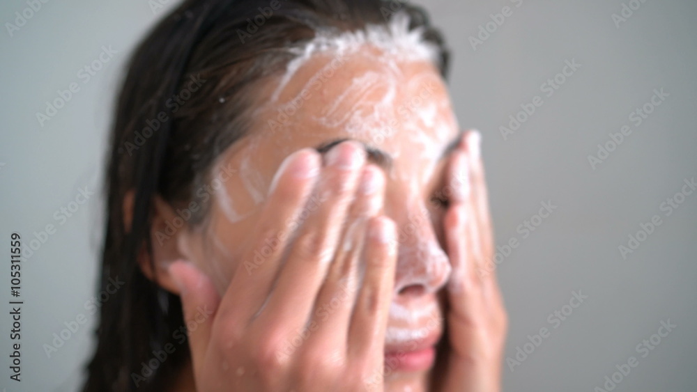 Skincare woman washing scrubbing face with facewash soap scrub in hot water shower. Closeup of Asian female young adult face cleaning skin.