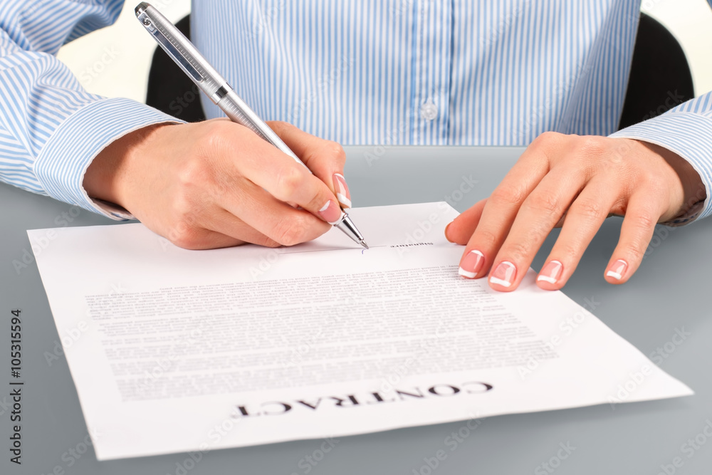 Female signing contract at desk. Female signing contract at desk.