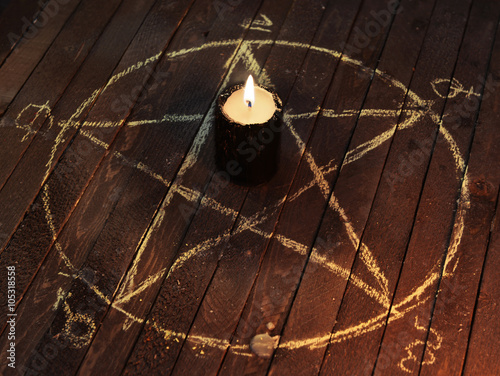 Photography Black candle in pentagram on wooden planks