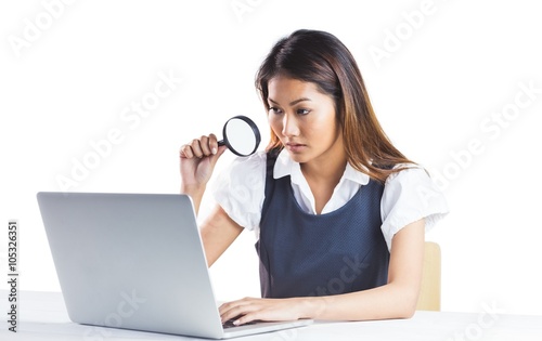 Businesswoman looking through magnifying glass and using laptop