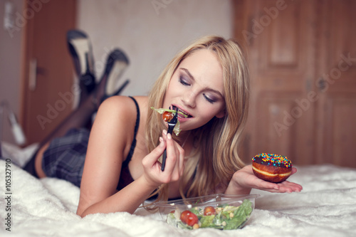 Woman eating salad and holding donut
