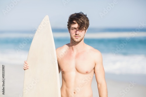 Handsome man holding surfboard on the beach