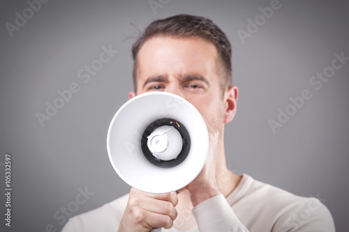 Young man screaming with a megaphone on grey background