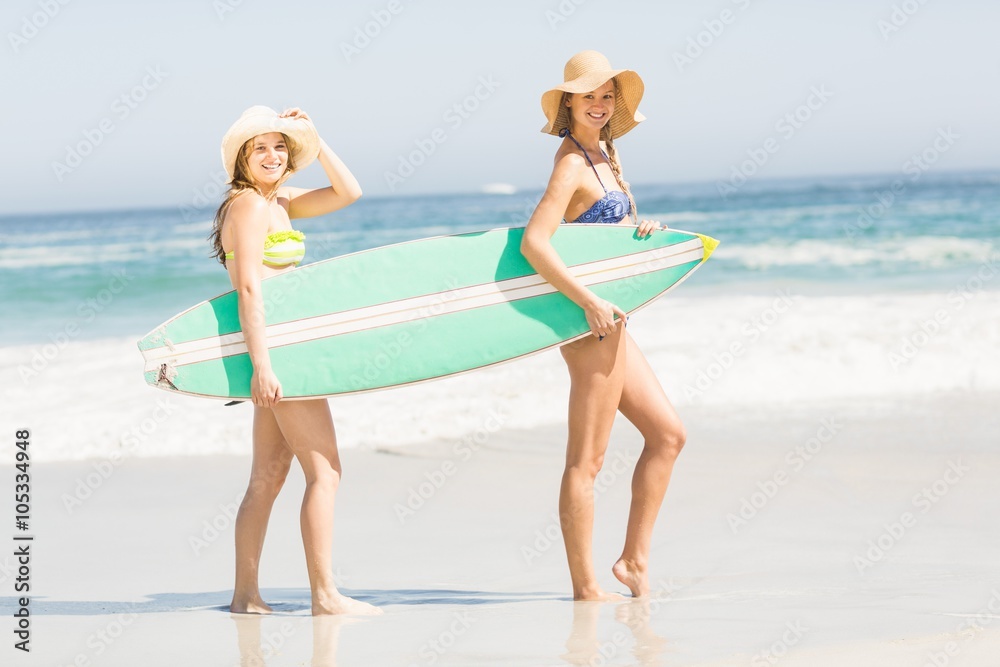 Two women carrying surfboard on the beach