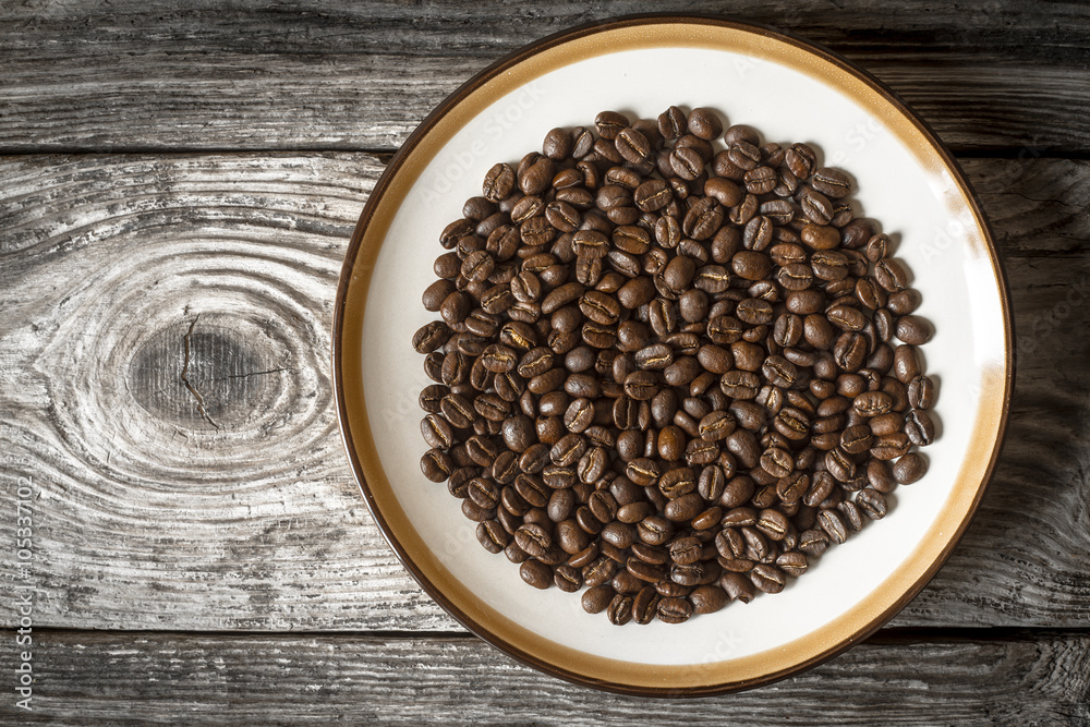 Fototapeta premium Coffee beans on the plate on the wooden table top view
