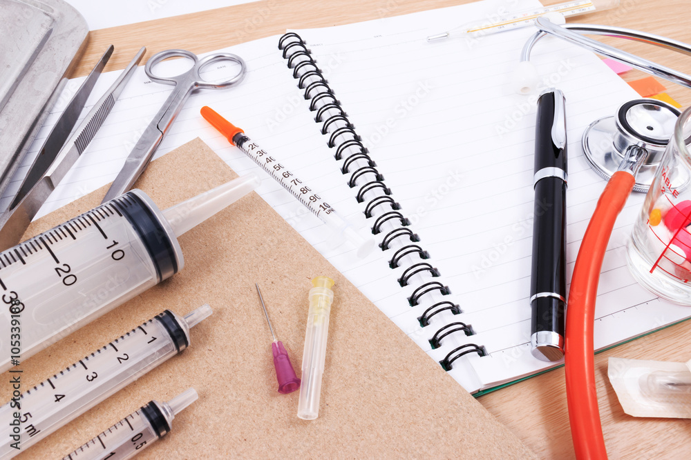 Stethoscope, syringes, scissors, pen and forceps on a white medical work surface. Stethoscope, syringes, scissors, pen and forceps on a white medical work surface.