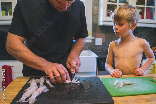 Boy watching man cleaning squid in kitchen photo