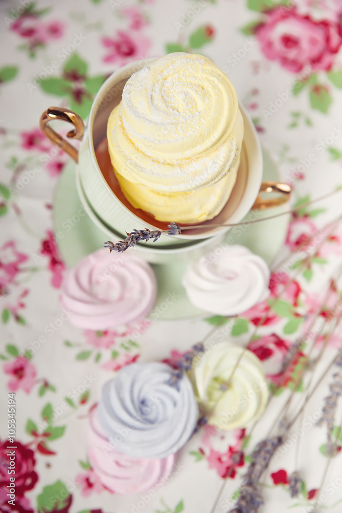 Small spiral meringues on the tablecloth with a floral pattern. Toned image. Pastel colored. Top view Small spiral meringues on the tablecloth with a floral pattern. Toned image. Pastel colored. Top view