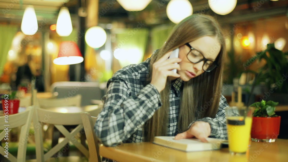 Girl in glasses and plaid shirt talking on cellphone while sitting in the cafe
Girl in glasses and plaid shirt talking on cellphone while sitting in the cafe